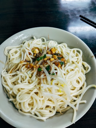 A steaming hot bowl of noodles garnished with sesame seeds and green onions.