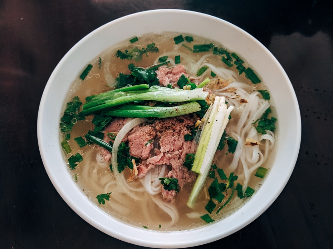 A steaming bowl of pho ga with rice noodles, shredded chicken, Thai basil, and lime