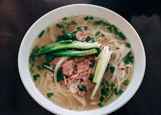 white noodle soup with green leaf vegetable in white ceramic bowl