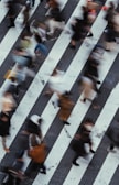 A blurred motion shot of a busy street corner with pedestrians crossing under city lights.