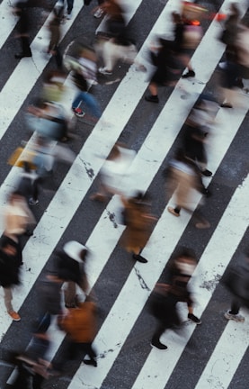 A blurred motion shot of a busy street corner with pedestrians crossing under city lights.