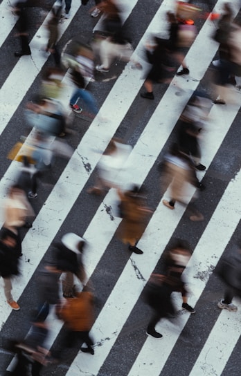 Blurred motion captures a busy street crossing with numerous pedestrians in mid-step, walking in various directions across marked crosswalk lines.