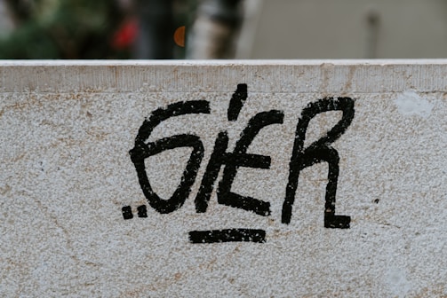Black graffiti text is spray-painted on a light-colored stone wall. The wall has a textured surface with visible signs of wear and small cracks.