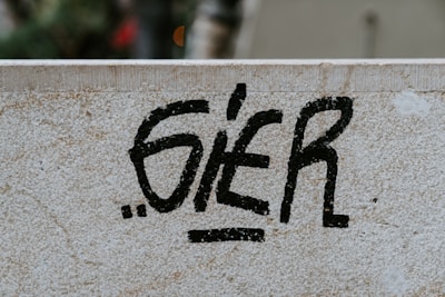 Black graffiti text is spray-painted on a light-colored stone wall. The wall has a textured surface with visible signs of wear and small cracks.