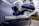 A close-up side view of a blue hybrid car, focusing on the side mirror and the 'HYBRID' badge. The background is slightly blurred, highlighting the details of the vehicle.