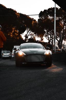 A sleek black luxury car waiting at a city curb under soft evening lights.