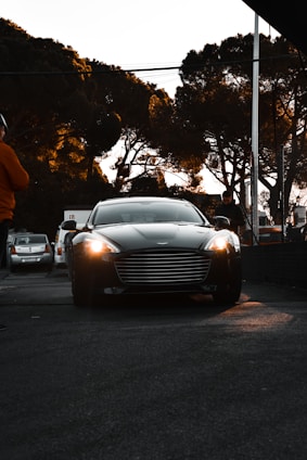 A sleek black luxury car with gold accents parked in front of an airport terminal at sunset.