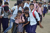 Smiling students in uniform holding books and backpacks outside the school building.