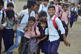 Smiling students in uniform holding books and backpacks outside the school building.
