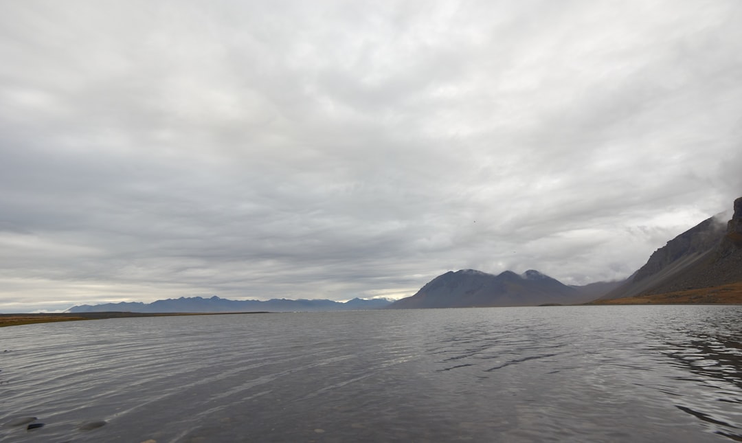 body of water near mountain under cloudy sky during daytime