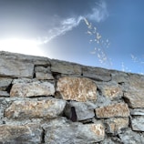 Photo of a freshly built stone wall with clean mortar lines under a bright sky.