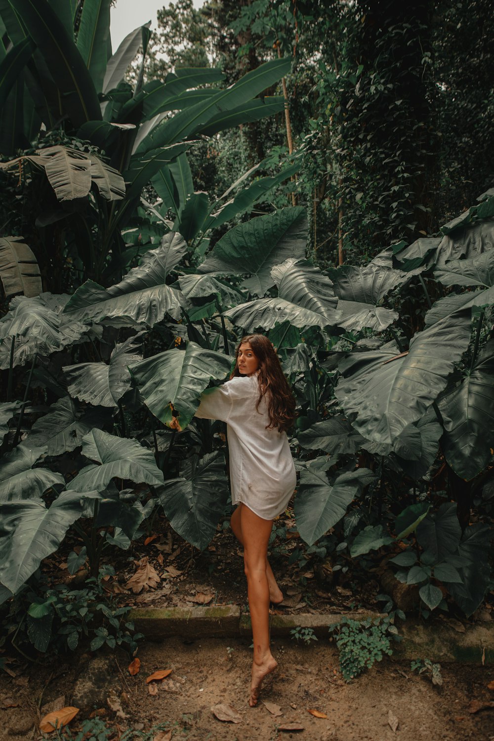woman in white long sleeve shirt standing in the middle of green leaves