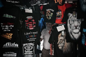 A variety of T-shirts are displayed with humorous and bold text designs, featuring phrases like 'I don't need Google,' and graphics such as lions and tigers. The T-shirts are predominantly dark with bright text and images.
