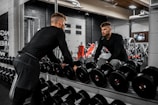 man in black long sleeve shirt and black pants carrying black dumbbell