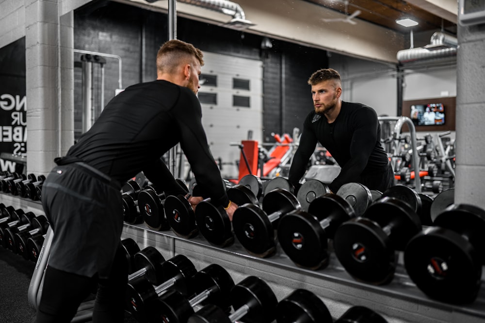 man in black long sleeve shirt and black pants carrying black dumbbell