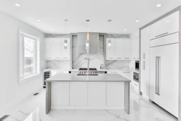 A modern kitchen with marble countertops, warm lighting, and custom cabinetry.