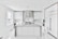 A modern, sleek kitchen featuring minimalist design with white cabinetry and marble countertops. The room includes stainless steel appliances, hanging pendant lights, and a large central island. Large windows provide ample natural light.
