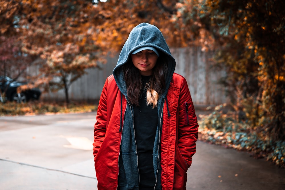 woman in red and black jacket standing on road during daytime