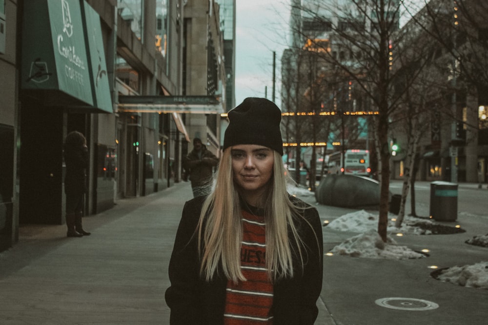 woman in black coat standing on sidewalk during daytime