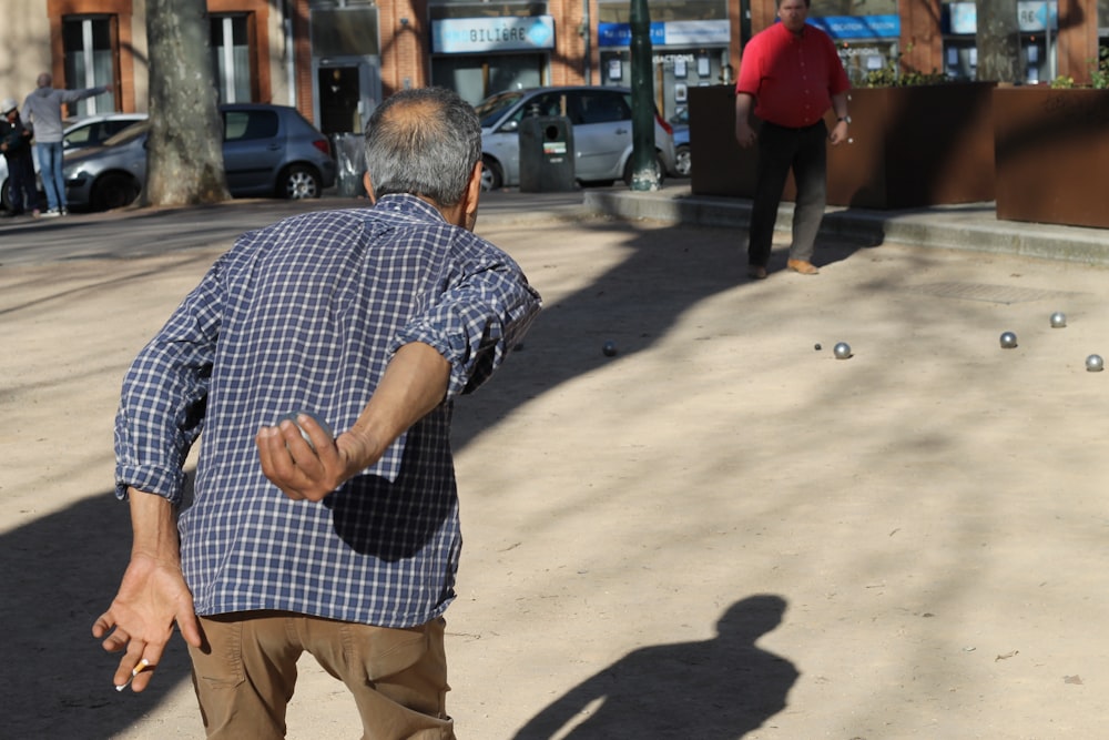 黒と白の市松模様のボタンアップシャツと茶色のズボンを着た男が歩道に立っています