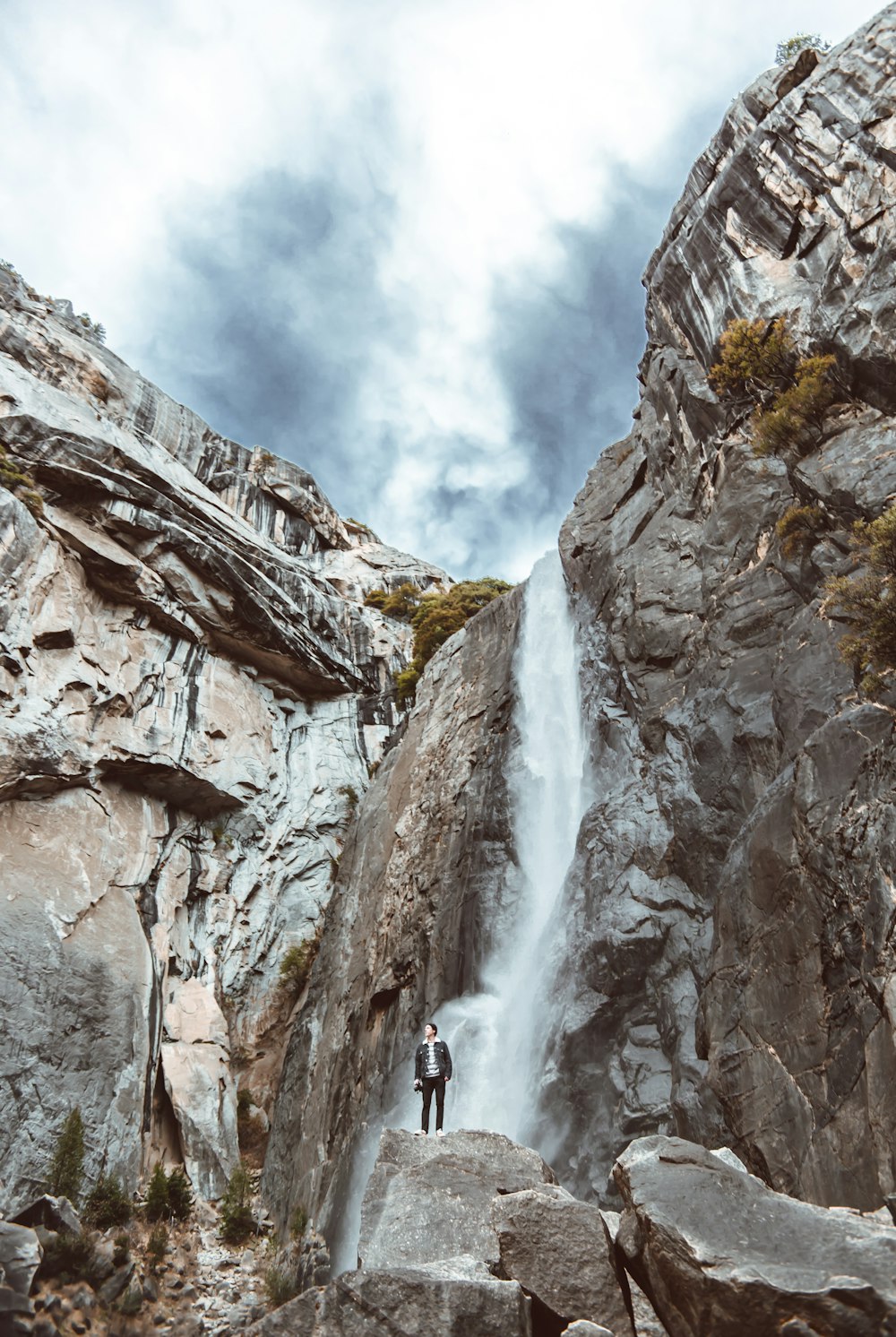 person in black jacket standing on rocky mountain under white cloudy sky during daytime