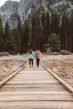 Couple hiking hand-in-hand along a sunlit mountain trail surrounded by vibrant wildflowers.