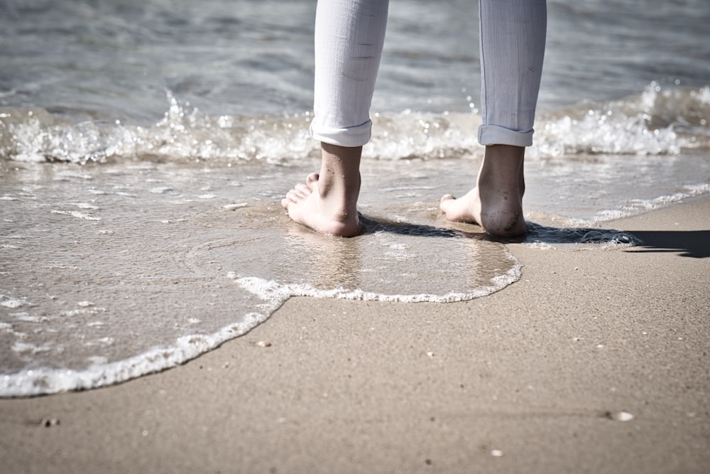 person in white pants standing on beach shore during daytime