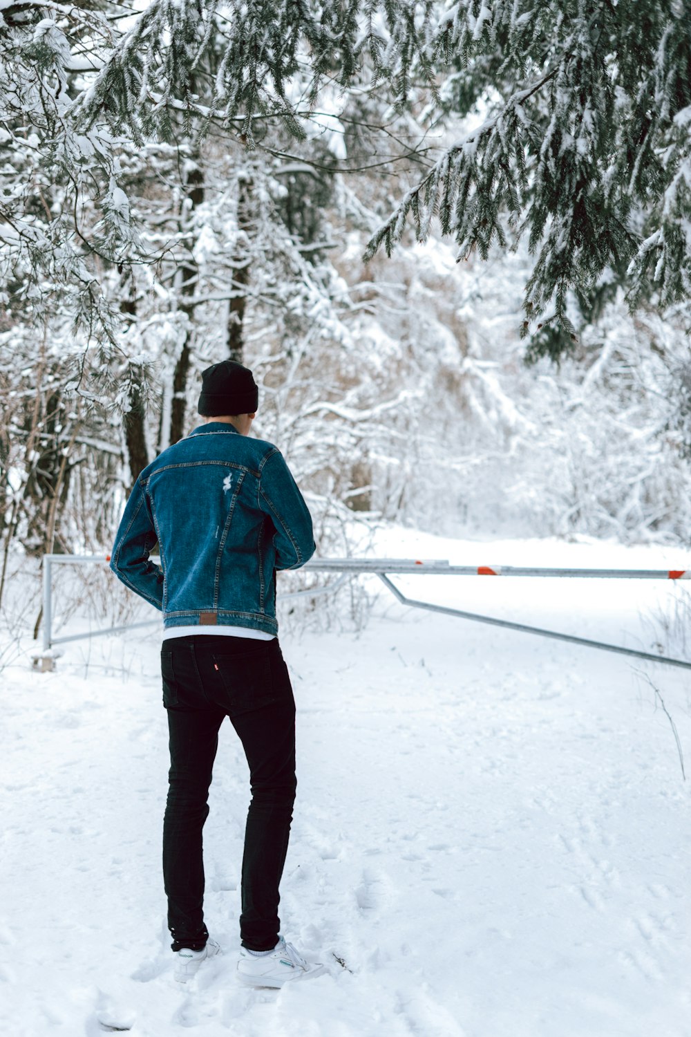 man in blue jacket and black pants standing on snow covered ground during daytime