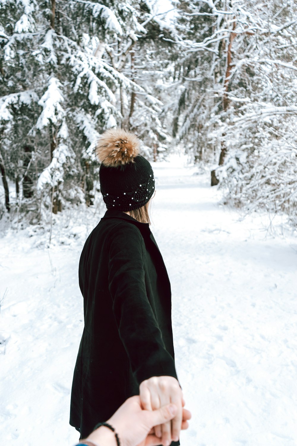 昼間、雪に覆われた地面に立つ黒いジャケットを着た人