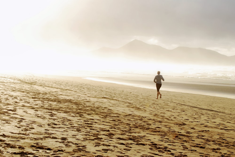 woman in white shirt and black shorts walking on brown sand during daytime