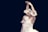 A ballet dancer is performing with arms gracefully raised above her head. She wears a white tutu adorned with delicate lace and sparkling details. Another dancer is partially visible in the background, also dressed in a similar attire. The background is dark, emphasizing the elegance and poise of the dancers.