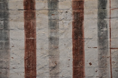 Vertical stripes of varying shades and textures are painted over a rough, textured wall. The surface shows signs of wear and age, with muted tones enhancing its rustic appearance.