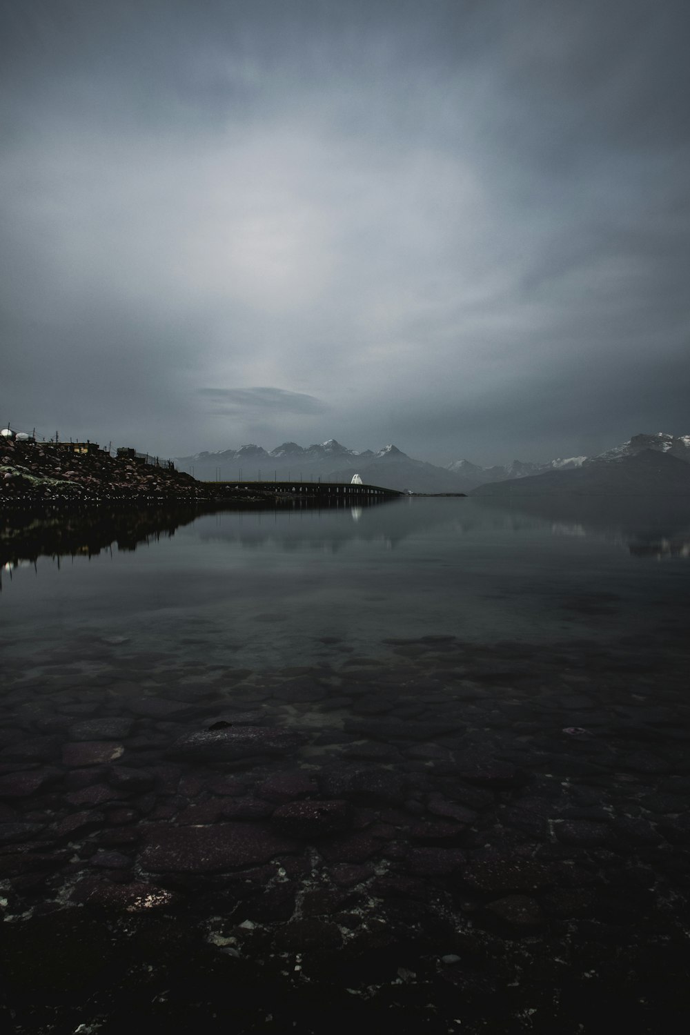 body of water near mountain under cloudy sky during daytime