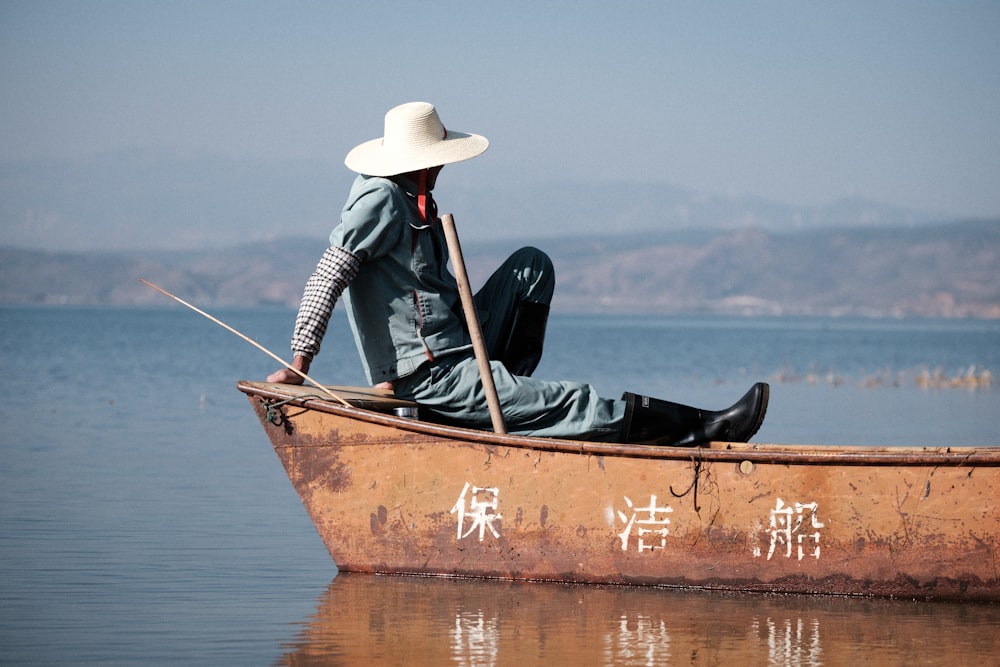 man in brown hat and black jacket riding on brown boat during daytime