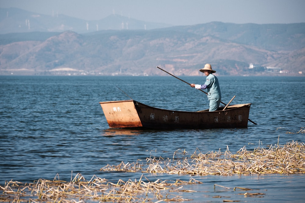 man in white shirt and black pants sitting on brown wooden boat on sea during daytime