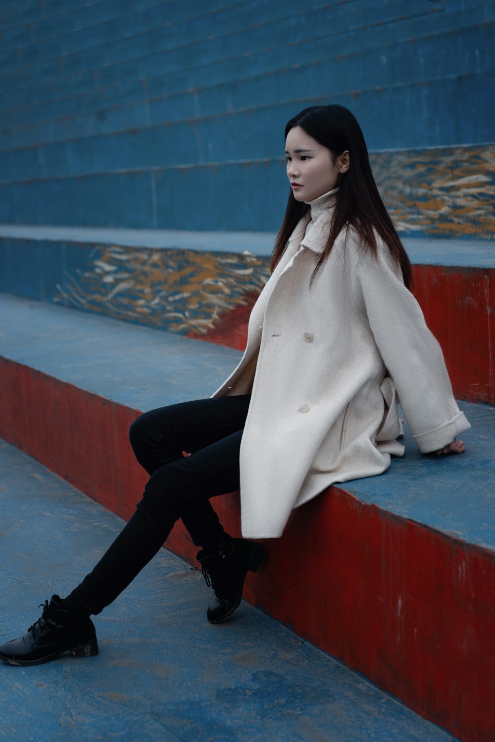 woman in white coat and black pants sitting on red concrete bench