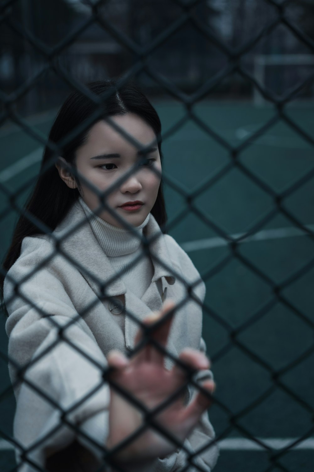 woman in white sweater standing beside blue metal fence during daytime