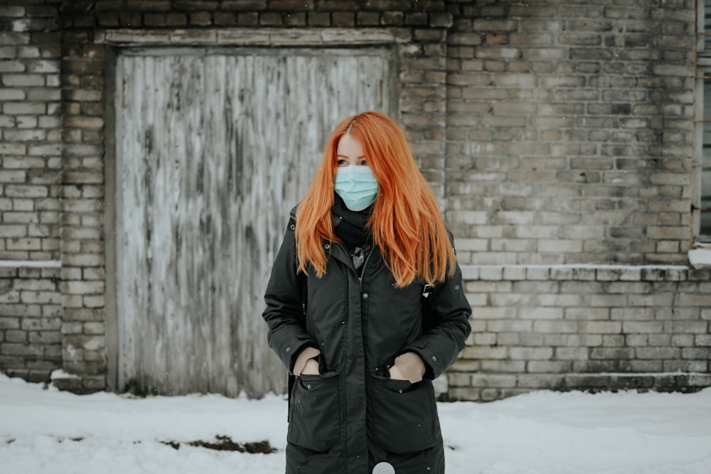 woman in black coat standing near brown brick wall