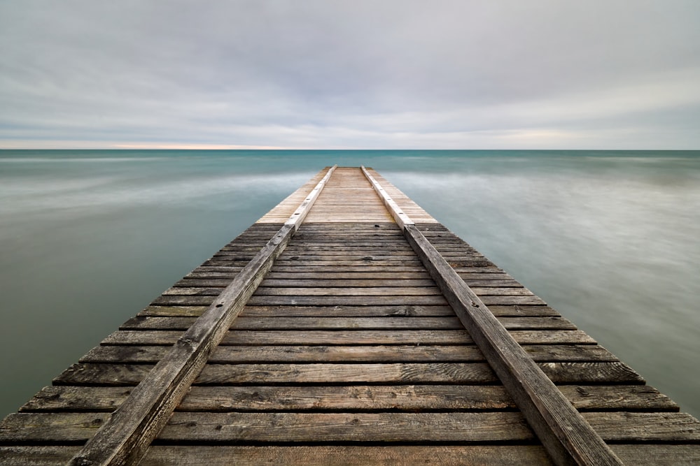 brown wooden dock on body of water under cloudy sky during daytime