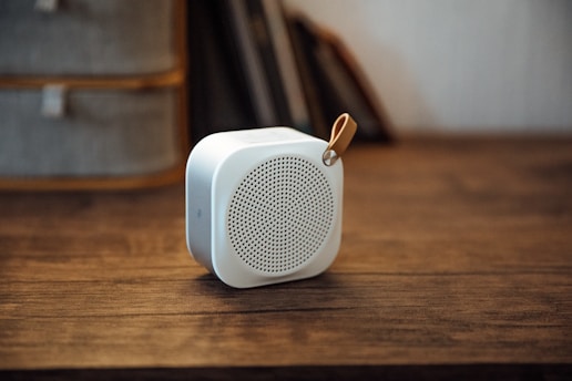 Close-up of a sleek, compact high-fidelity speaker with glowing blue accents on a wooden desk.