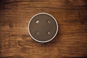 A top-down view of a circular smart speaker with buttons on its surface, placed on a wooden background.