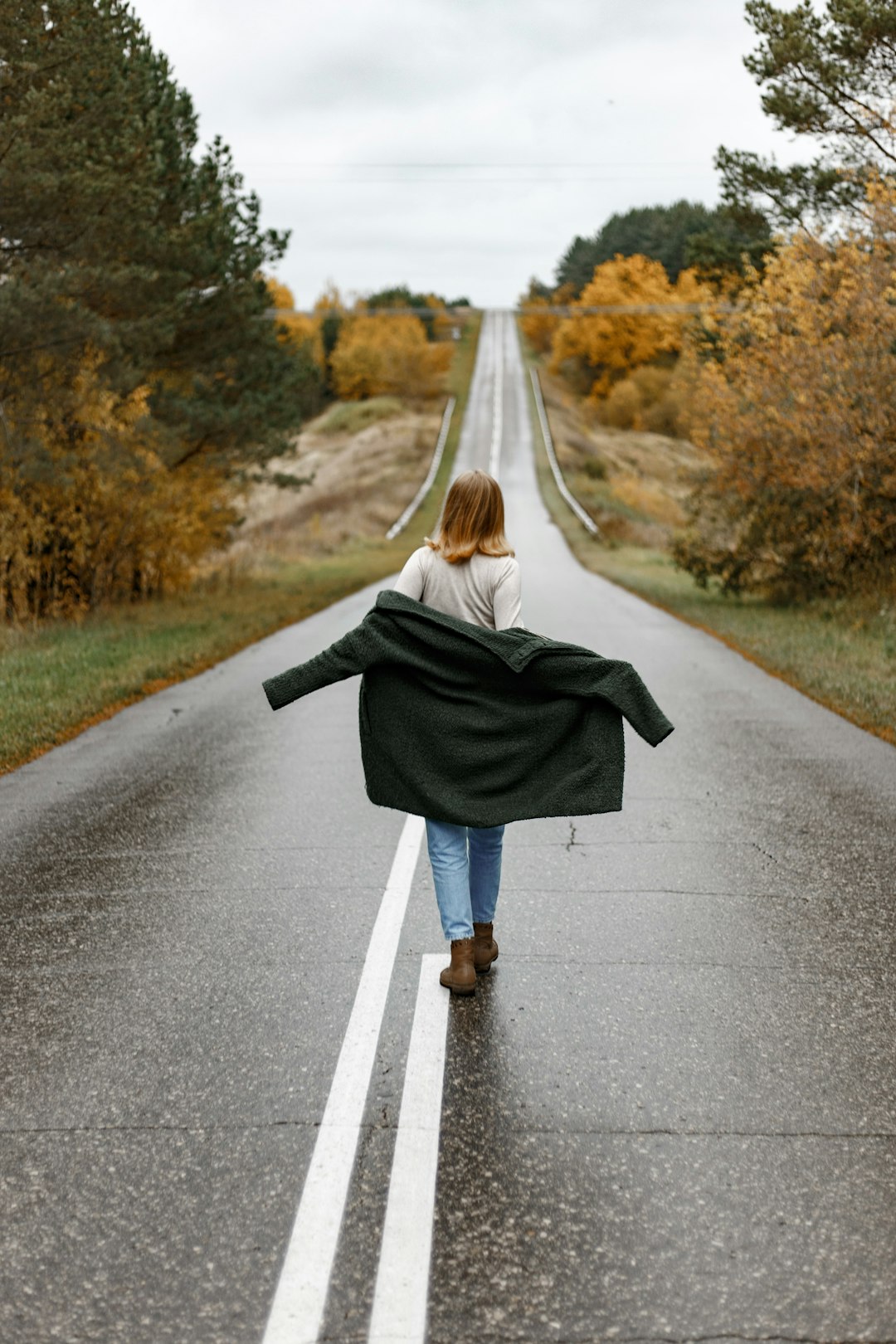 woman in black coat standing on gray asphalt road during daytime