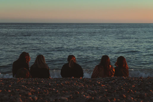 3 women sitting on seashore during daytime
