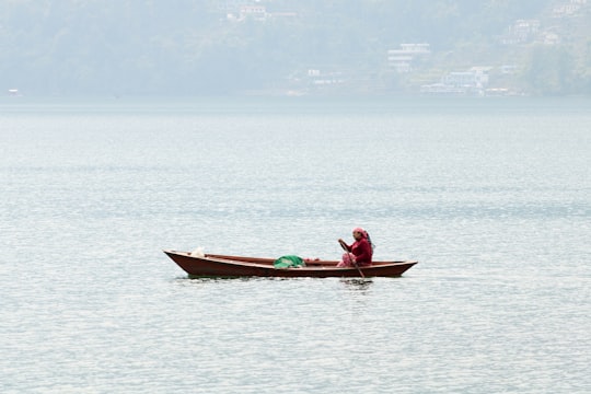 man in red shirt riding on red boat during daytime in Pokhara Nepal