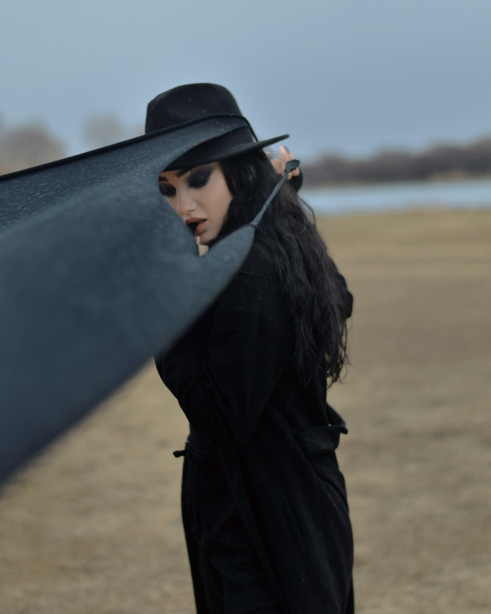 woman in black coat and black hat standing on brown field during daytime