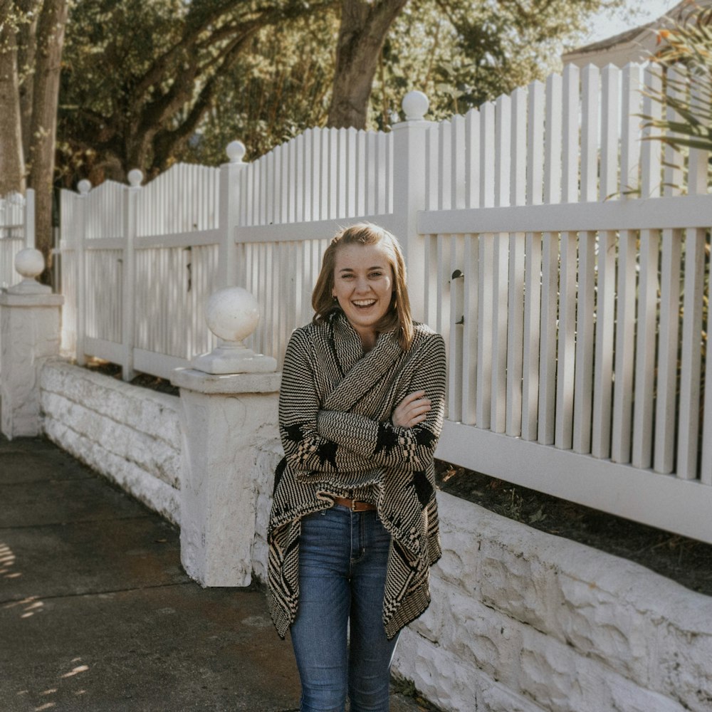 woman in black and white scarf and blue denim jeans standing beside white wooden fence during