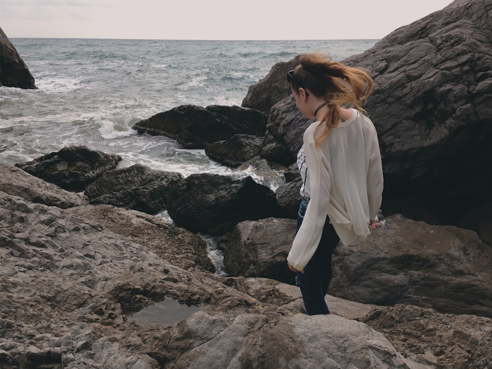 woman in white long sleeve shirt standing on rock formation near sea during daytime