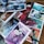 Several open comic book pages are laid out on a wooden surface, showcasing vibrant, futuristic scenes and characters. Speech bubbles contain dialogues, and the art style is colorful and dynamic. Characters appear to be in a space or sci-fi setting.
