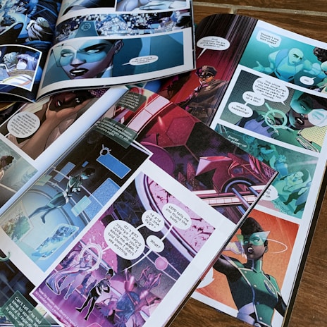 Several open comic book pages are laid out on a wooden surface, showcasing vibrant, futuristic scenes and characters. Speech bubbles contain dialogues, and the art style is colorful and dynamic. Characters appear to be in a space or sci-fi setting.