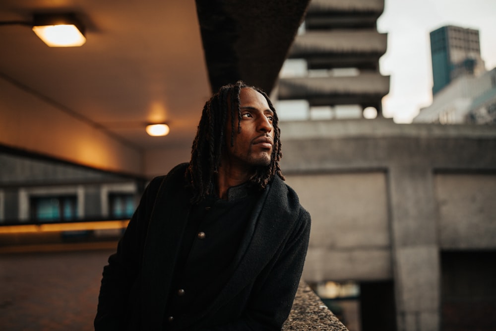 man in black button up jacket standing near brown concrete wall